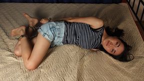 Carrie: barefoot girl in tank top and jeans shorts, hogcuffed with shiny steel cuffs, rolls and wriggles on the bed (HD MOV)